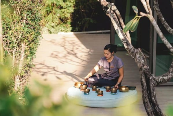 Una persona sentada sobre un cojín circular al aire libre, con varios cuencos.