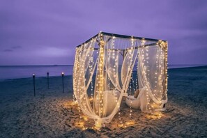A beach tent with a canopy and string lights, surrounded by sand.