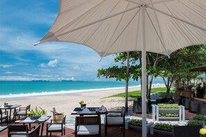 A beachside dining area with tables and chairs under a large umbrella, overlooking the ocean. - Layana Resort & Spa (Koh Lanta)