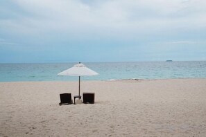 Een strand met twee stoelen en een witte parasol.
