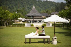 A massage therapy session on a grassy lawn with a traditional building in the background. - Layana Resort & Spa (Koh Lanta)