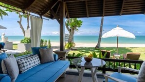 A covered outdoor seating area with a view of the beach, a blue sofa, a small table, and a white umbrella. - Layana Resort & Spa (Koh Lanta)