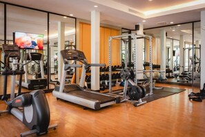 A gym with treadmills, weight machines, and a television screen.