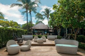A wooden deck with wicker furniture, palm trees, and a building in the background. - Layana Resort & Spa (Koh Lanta)