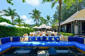 A poolside lounge area with blue seating, palm trees, and a building in the background. - Layana Resort & Spa (Koh Lanta)