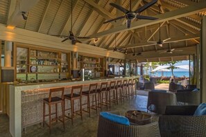 Een bar met een lange toonbank, meerdere barkrukken en een plafondventilator.