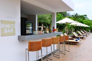 Un espace bar avec une enseigne indiquant « WHITE BAR » et une rangée de chaises longues ombragées par des parasols.