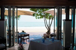 A dining area with a table set for two, overlooking a beach.