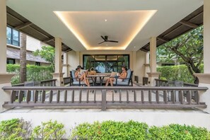 An outdoor seating area with a table and chairs, surrounded by a railing, and a ceiling fan above.