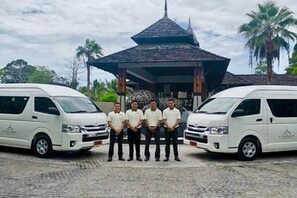 A group of people standing between two white vans in front of a building with a distinctive roof structure. - Layana Resort & Spa (Koh Lanta)