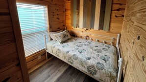 A wooden cabin room with a bed, wooden walls, and a window with blinds. - Cozy Cabins-Pet friendly, newly renovated, WiFi, kitchen, 2 bedroom  (Steinhatchee)