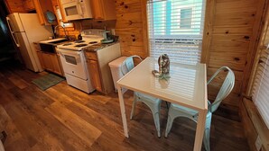 A compact kitchen with wooden cabinets, a microwave, a stove, and a dining table with chairs. - Cozy Cabins-Pet friendly, newly renovated, WiFi, kitchen, 2 bedroom  (Steinhatchee)