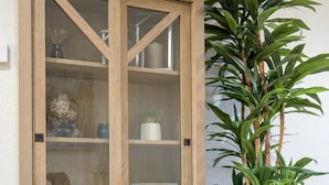 A wooden display cabinet with glass doors, a small white shelf, and a single drawer.