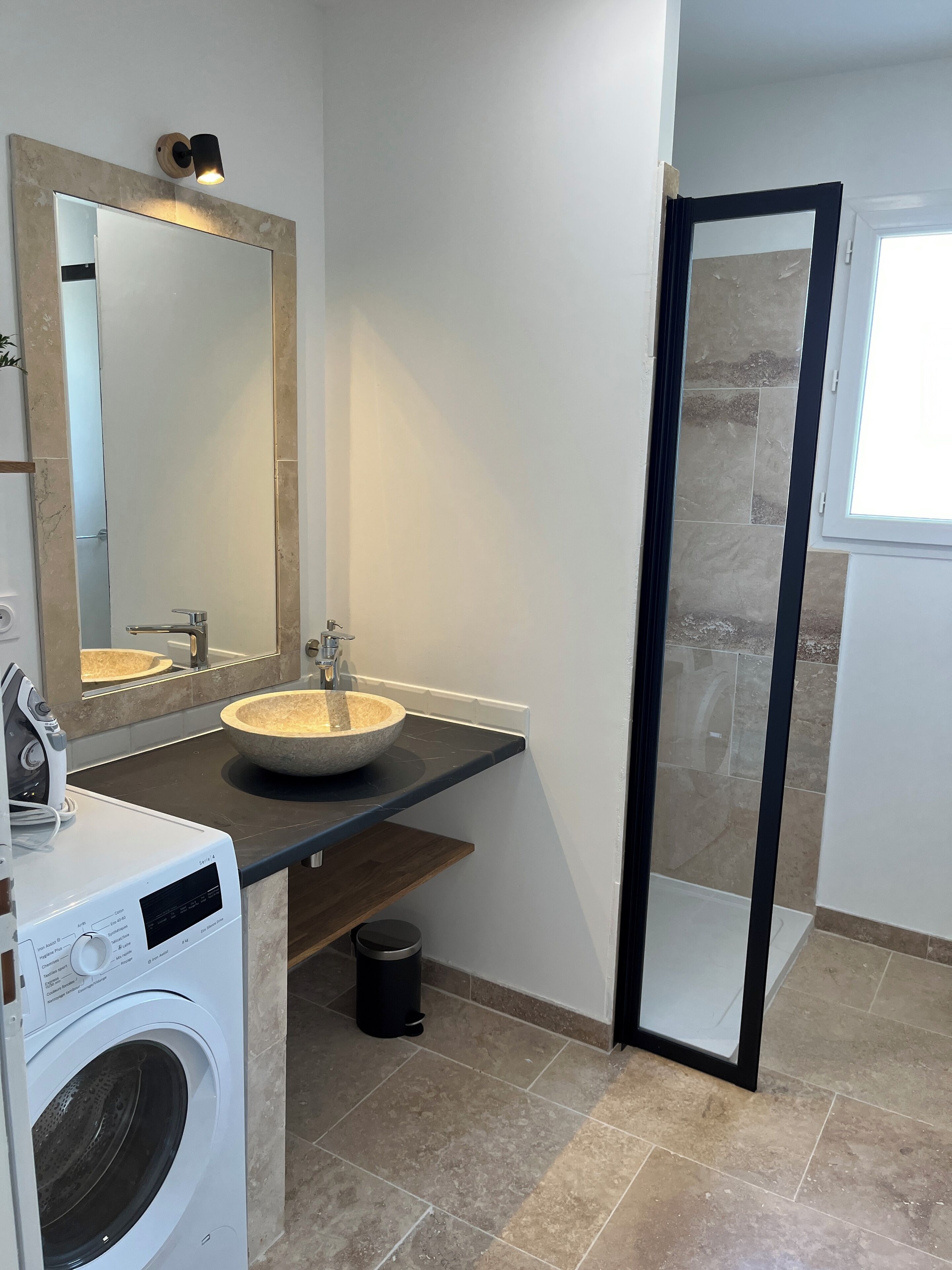 Uma casa de banho moderna com um espelho grande, uma pia, uma máquina de lavar roupa e zona de duche.