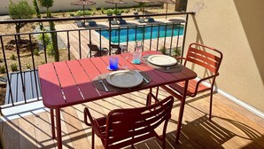 Ein Balkon mit Tisch für zwei Personen, mit Blick auf einen Swimmingpool und ein Gebäude mit einem Ziegeldach.