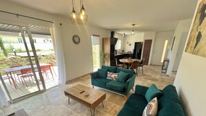 A spacious living area with a green sofa, a wooden coffee table, and a dining table with chairs. A kitchen is visible in the background.