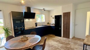 A modern kitchen with dark cabinetry, a black refrigerator, and a dining area with a round table and chairs.
