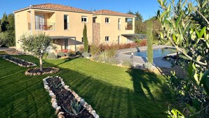 A two-story house with a tiled roof, a swimming pool, and a well-maintained garden.