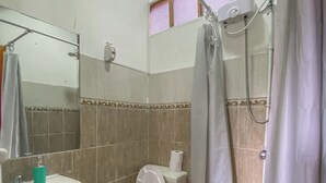 A bathroom with a toilet, sink, shower, and a window with pink blinds.