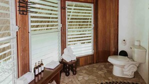 Een badkamer met betegelde vloer, houten wanden, een houten bankje en een toilet.