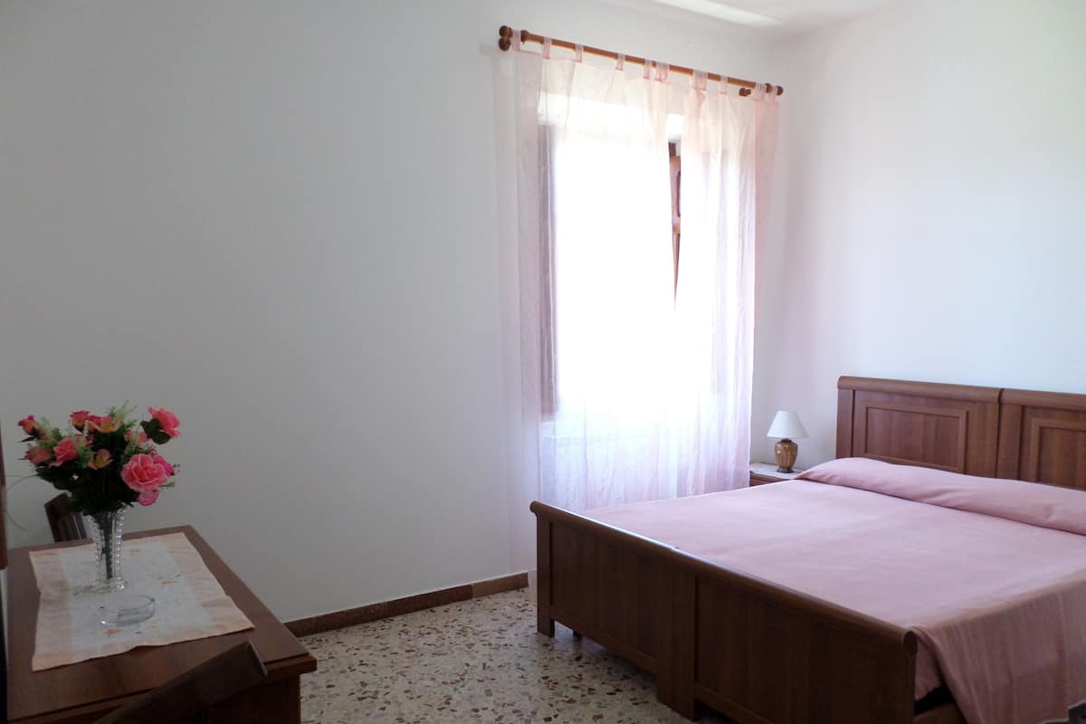 Una camera da letto con un letto, un comodino, una lampada e un vaso con fiori.