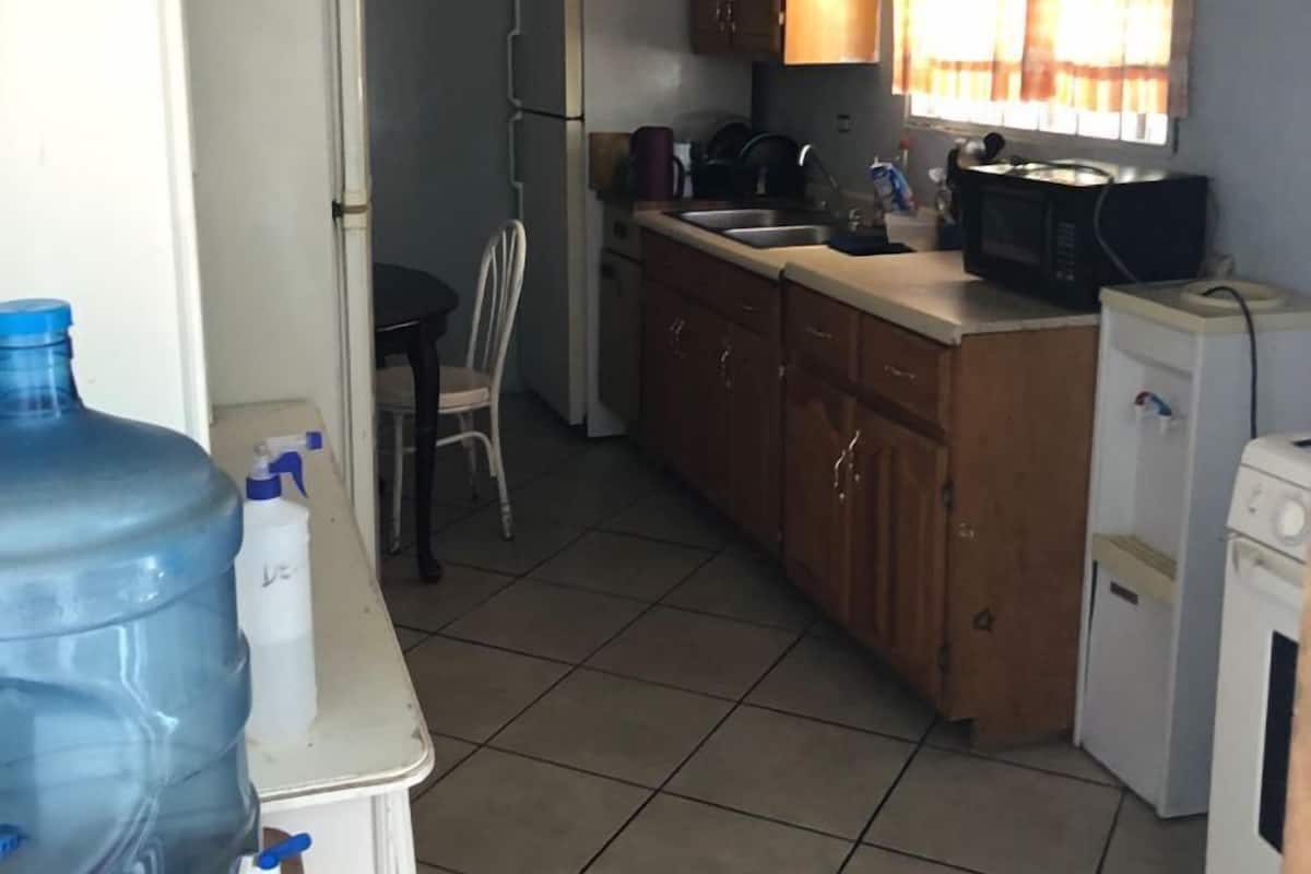 A compact kitchen with basic appliances, a water dispenser, and a chair.
