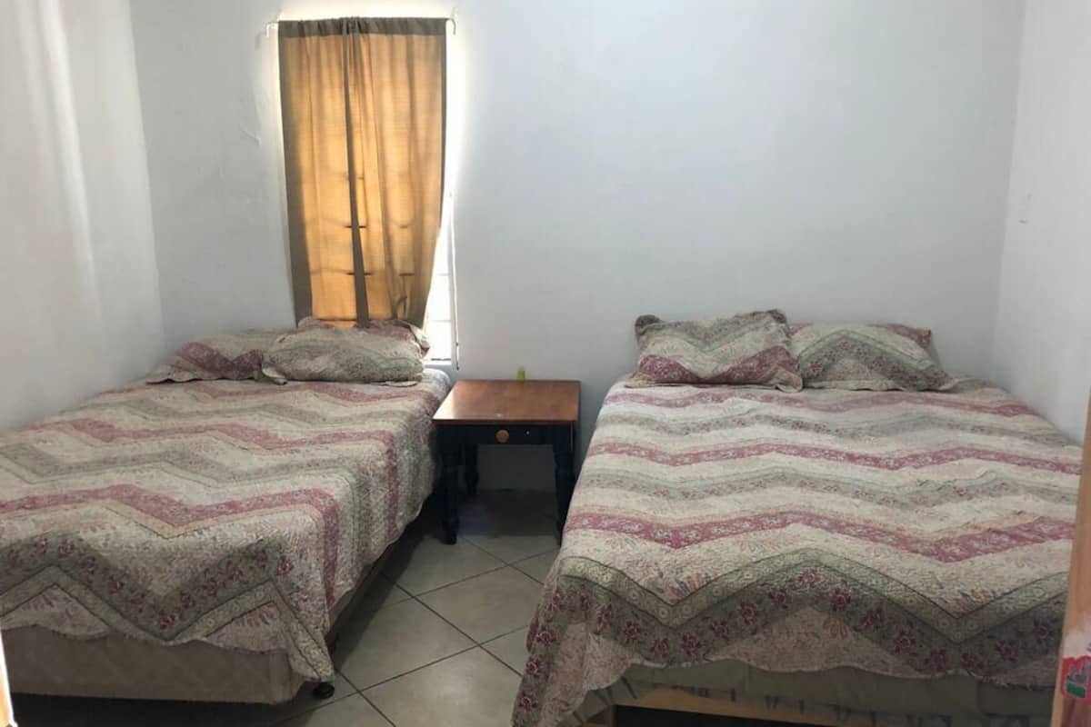 A bedroom with two single beds, a small table, and a window with curtains.