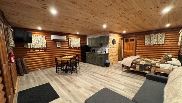 A log cabin interior with a dining area, kitchenette, and a sofa.