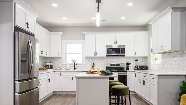 A modern kitchen with white cabinets, stainless steel appliances, and a central island with stools. - ATL Escape ~ Arcade I Fire pit I Patio! (Decatur)