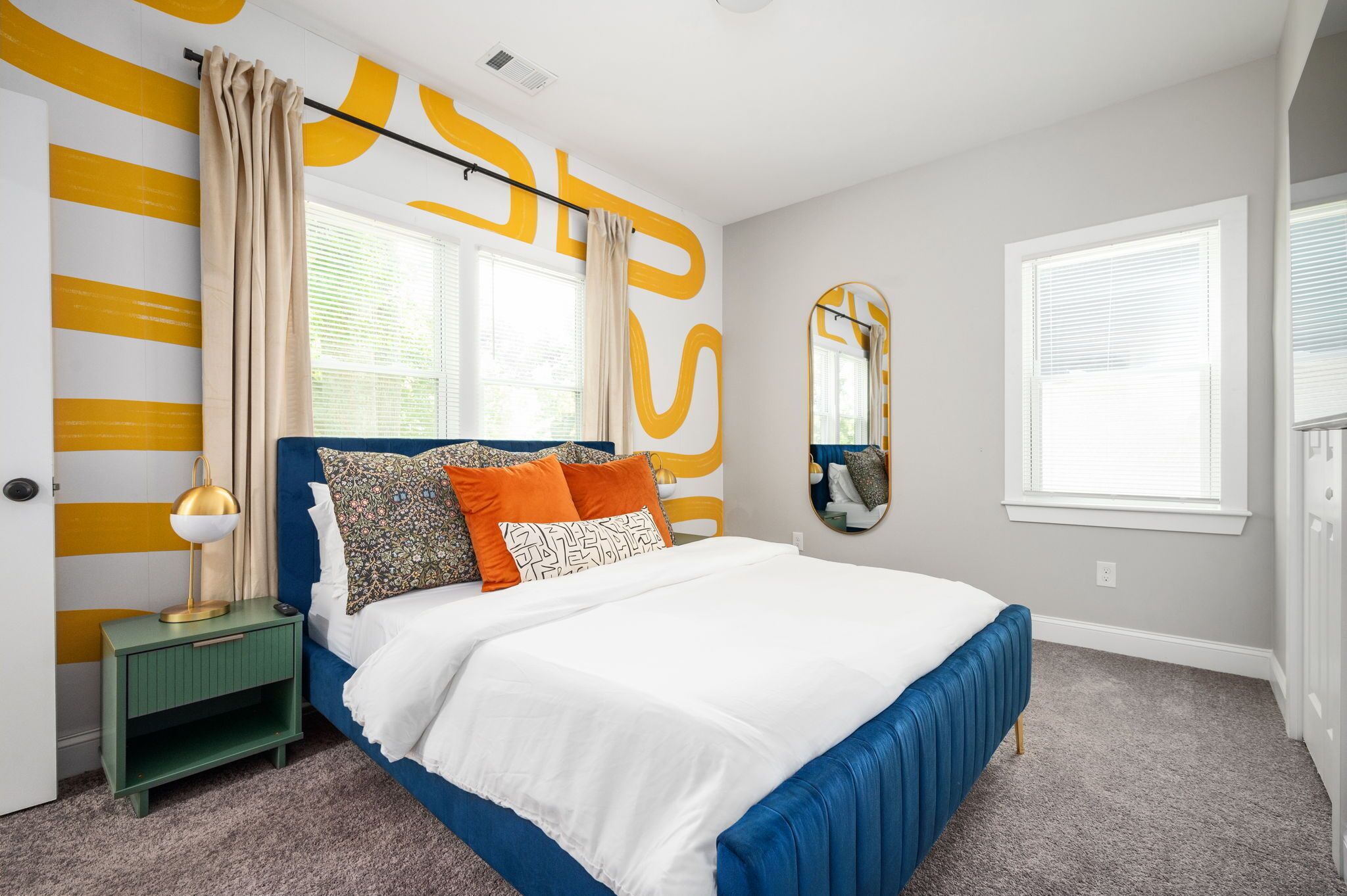 A bedroom with a bed, a nightstand, a mirror, and a window with blinds.