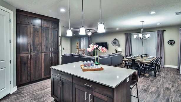 Una cocina moderna con armarios de madera oscura, una isla central con un recipiente de agua embotellada e iluminación colgante.