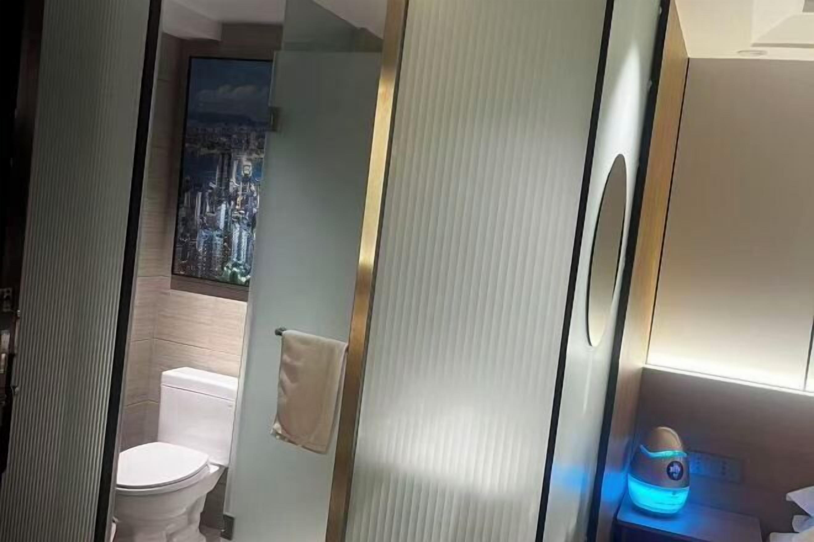 A bathroom with a toilet, a towel hanging on the wall, and a nightstand with a blue device.