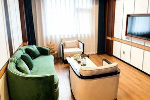 A modern living room with a green sofa, a beige armchair, a coffee table, and a flat-screen TV mounted on the wall. - Yatai Longda Hotel (Changchun)