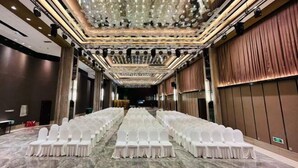 Un salón de conferencias con filas de sillas blancas, piso de mármol y una araña.