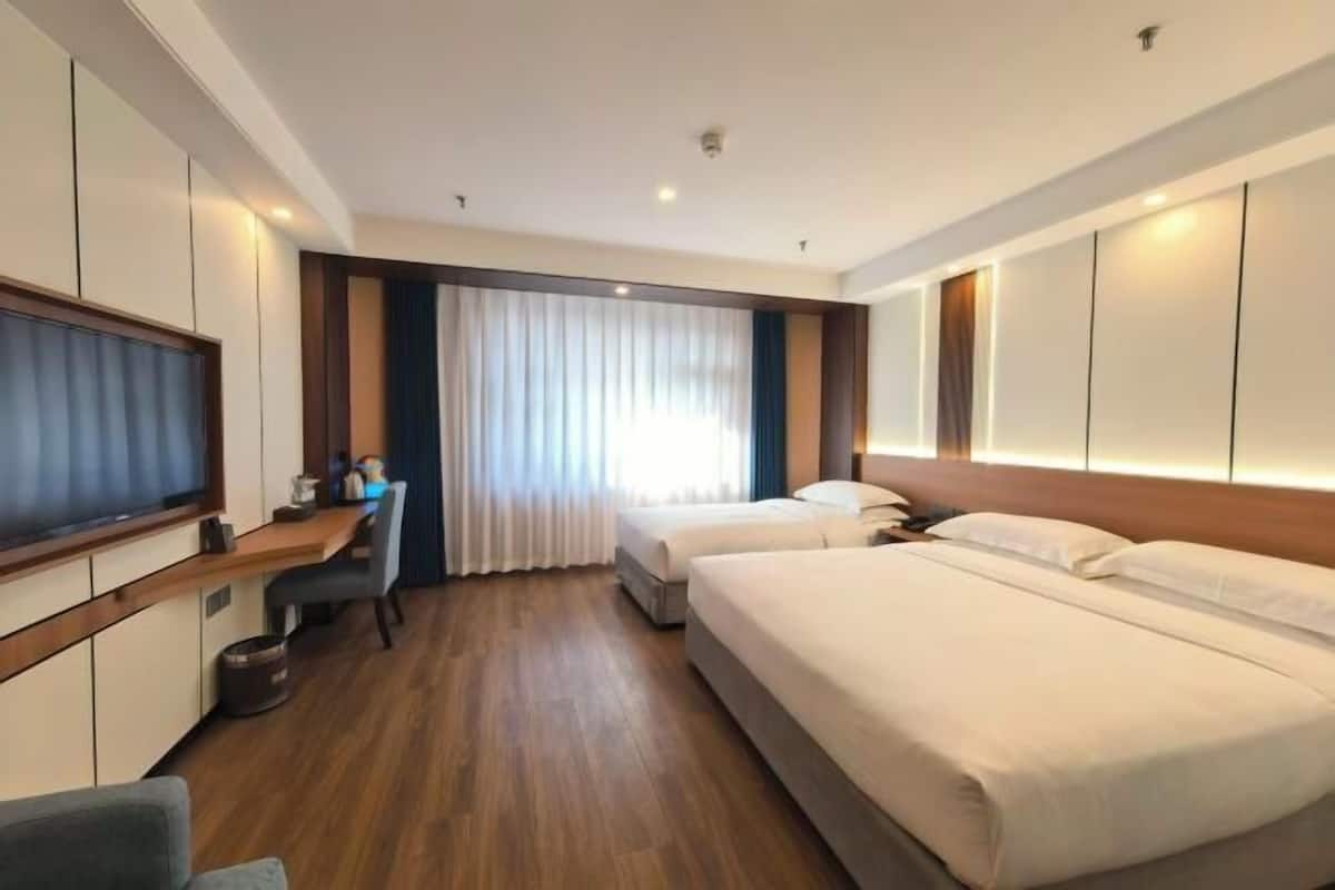 Habitación de hotel con cama, escritorio, televisor y ventana con cortinas.