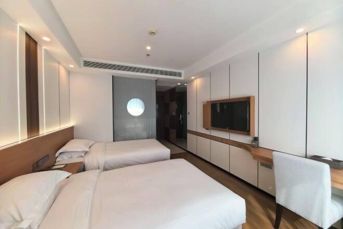 Habitación de hotel con dos camas, un escritorio, una silla, un televisor y un ventanal grande.