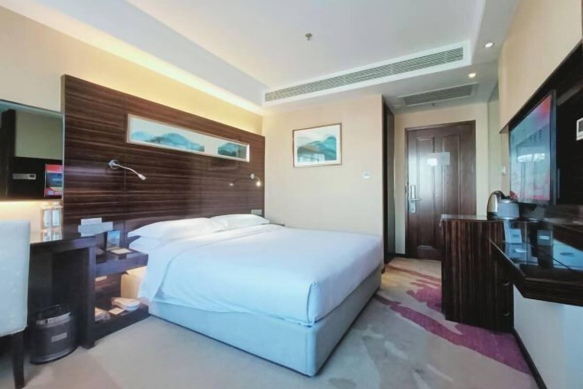 Una habitación de hotel con cama, mesita de noche, espejo y una obra de arte en la pared.