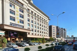 A hotel with multiple floors, a parking lot with several cars, and a clear sky. - Yatai Longda Hotel (Changchun)