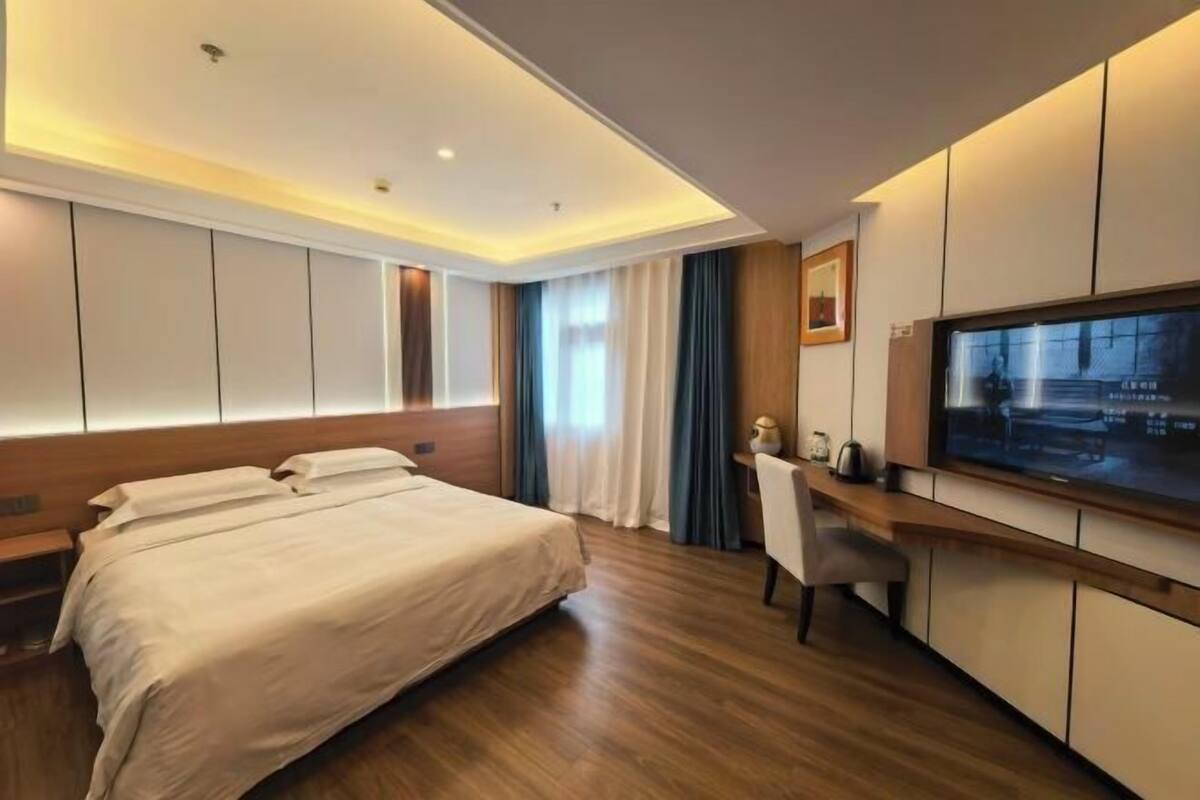 Una habitación de hotel moderna con una cama grande, un escritorio, un televisor y un ventanal con cortinas.