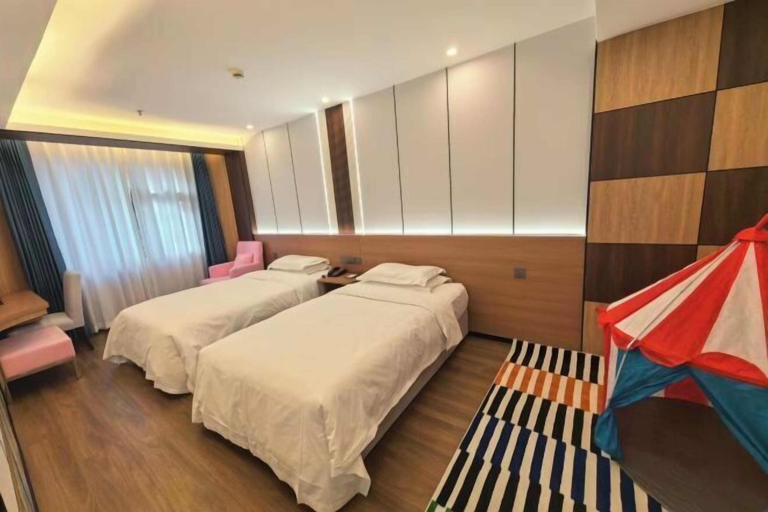 A hotel room with two beds, a wooden headboard, a striped rug, and a colorful kite decoration.