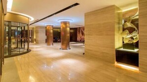 Un moderno vestíbulo de hotel con piso de madera pulida, amplias columnas cilíndricas y un separador de vidrio a la izquierda.