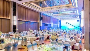 Un salón de banquetes con mesas redondas, manteles blancos y sillas con lazos azules.