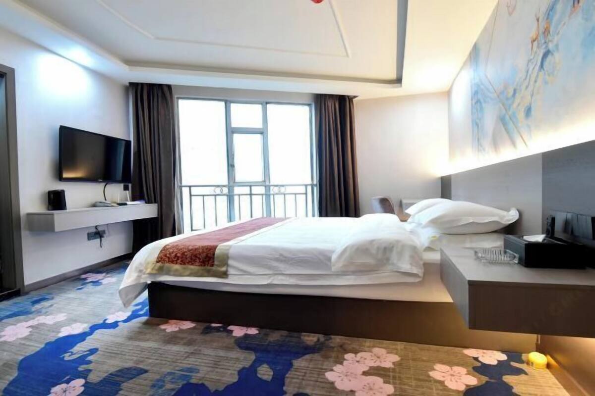 Una habitación de hotel con cama, televisión, escritorio y ventana con cortinas.