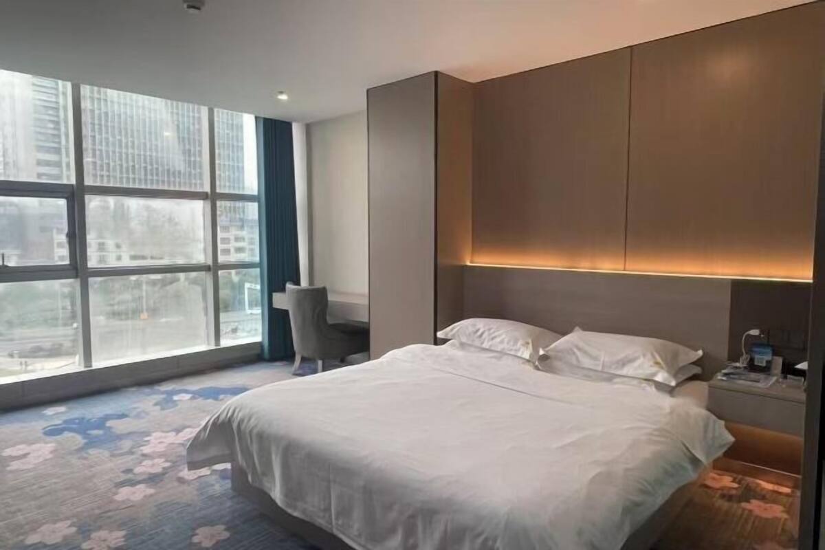 Una habitación de hotel con un ventanal grande, una cama, una silla y una mesita de noche.