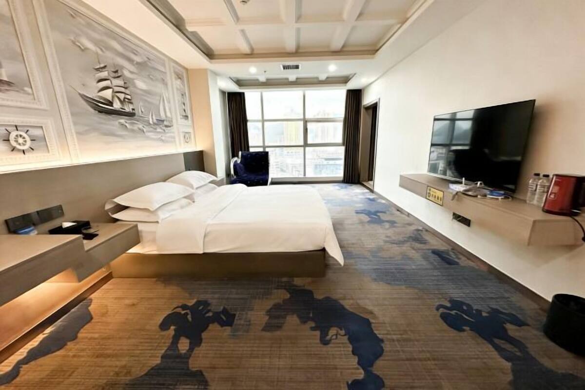 Habitación de hotel con una cama grande, televisión, escritorio y ventana con vista a la ciudad.