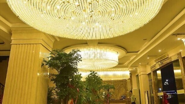 A grand chandelier in a hotel lobby with columns and a reception desk. - Huangshi Hotel (Anshun)