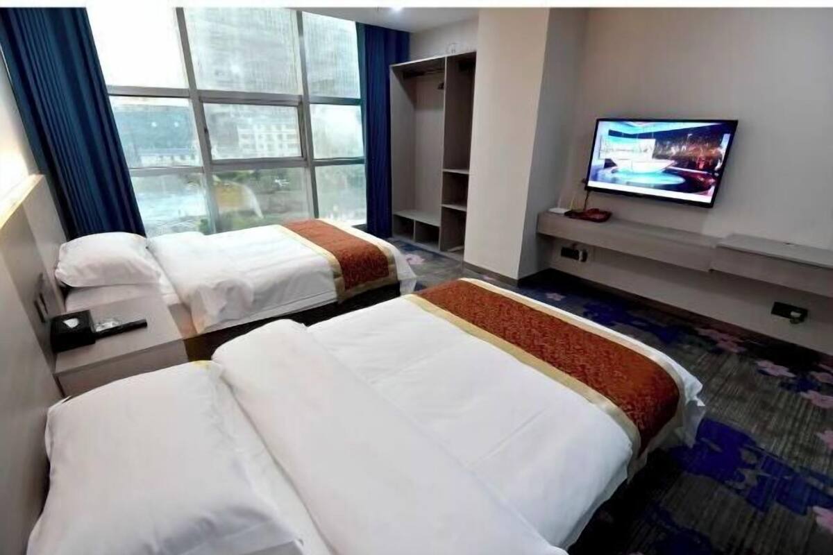 Habitación de hotel con dos camas, televisión, armario y ventana con vistas a edificios.