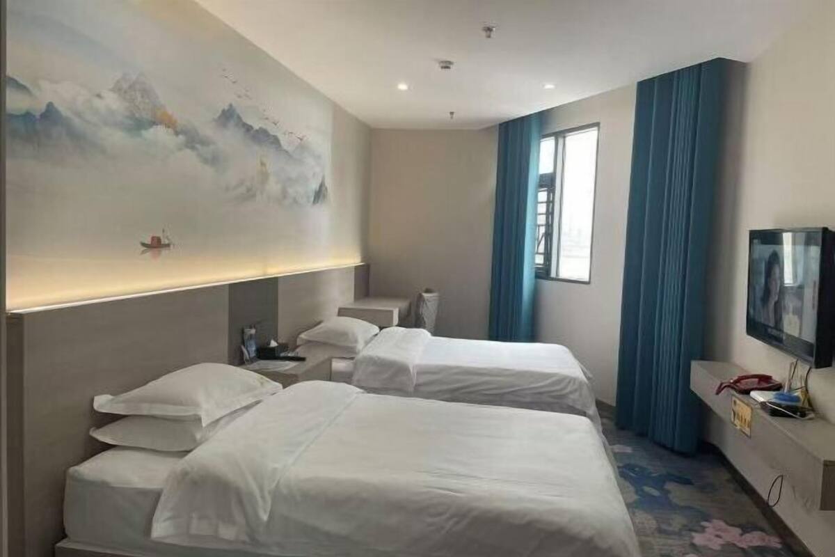 Habitación de hotel con dos camas, un cuadro en la pared, un televisor a la derecha y una ventana con cortinas.