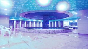 A modern indoor pool area with a central circular water feature, surrounded by a tiled floor and a few plastic chairs. - Huangshi Hotel (Anshun)