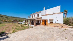 Una casa bianca con un patio in pietra, un pergolato in legno e una piscina sullo sfondo.